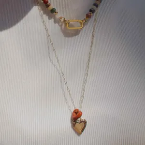 Detailopname van een gelaagde ketting met gekleurde kralen en hartvormige hanger