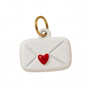 Dettaglio macro di un ciondolo a busta con cuore in smalto bianco e anello oro