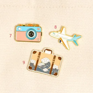 Detail of travel-themed enamel pins with a camera, airplane, and wave-print suitcase.