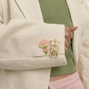 Detail view of pearl flower and enamel bouquet brooches on a linen blazer sleeve
