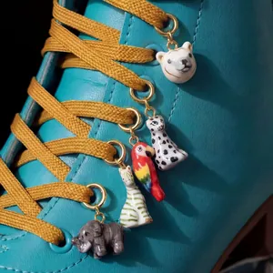 Dettaglio di ciondoli per scarpe in ceramica a forma di animale su uno stivale verde acqua.