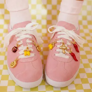 Gros plan de charms DIY fruits et insectes dorés sur des lacets roses.
