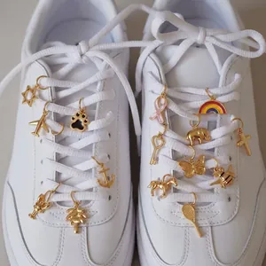 Detailansicht verschiedener goldfarbener Edelstahlanhänger an weißen Turnschuhschnürsenkeln.