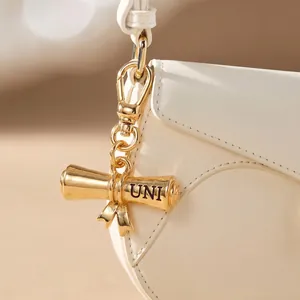 Detailed view of gold metal graduation scroll pendant with UNI engraving on a white bag