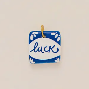 Dettaglio macro di un ciondolo quadrato in ceramica blu e bianca con scritta luck