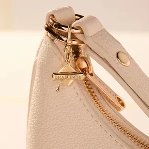 Close-up of gold graduation cap and scroll metal pendant on a white leather bag.