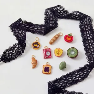 Macro view of miniature fruit and food charms collection with elegant black lace accent.