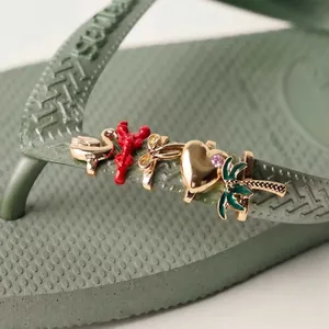 Detailaufnahme verschiedener goldfarbener Charms auf einem grünen Flip-Flop-Riemen.