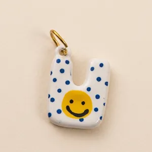 Gros plan d'un pendentif en émail blanc en forme de U avec pois bleus et smiley.