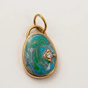 Gros plan d'un pendentif ovale plaqué or 18K avec des tourbillons d'émail bleu et vert