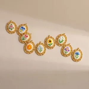 Detailed display of nine vintage embroidered flower pendants with gold filigree frames