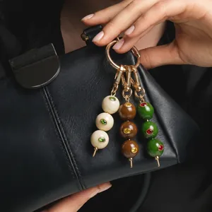 Detail van stijlvolle olijfvormige tassenhangers in drie kleuren aan een zwart leren tas.