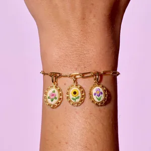 Close-up of pastoral style floral embroidery charms on a gold-toned chain bracelet
