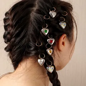 Dettaglio di ciondoli a cuore in acciaio inox con gemme colorate su capelli intrecciati.