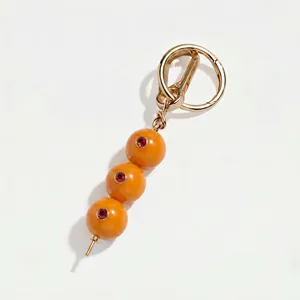 Detail van gouden sleutelhanger met drie oranje vruchtkralen en rode edelstenen.
