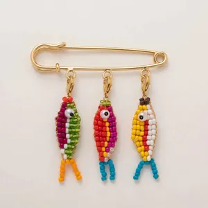 Close-up of colorful handmade beaded fish charms on 14k gold-plated safety pin brooch.