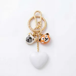 Close-up detail of cute dog and red panda enamel charms on a golden heart bag keychain