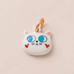 Détail rapproché d'un pendentif chat en émail blanc avec un anneau de bélière plaqué or