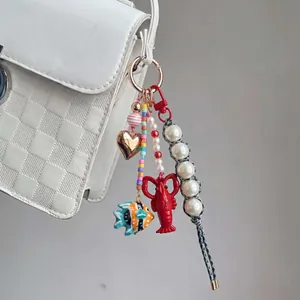 Primo piano di un ciondolo per borsa con perline, cuore dorato, aragosta e pesce