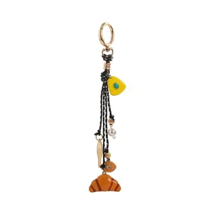 Detailed view of fashion bag charm with black cords and croissant pendant accessory