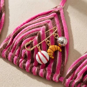Close-up of a decorative safety pin charm with baseball, croissant, and disco ball pendants