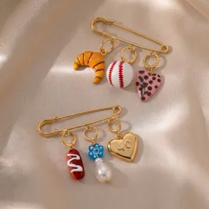 Detailed view of 18K gold-plated decorative safety pins with croissant and baseball charms.
