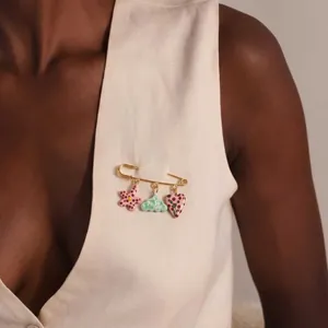 Close-up of golden safety pin brooch with flower, cloud and heart charms on vest