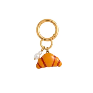 Detailed view of a golden croissant bag charm featuring a delicate white pearl accent.