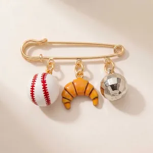 Detail view of gold-tone safety pin brooch with baseball, croissant, and disco ball charms