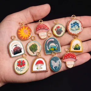 Detailed view of colorful enameled pendants with sun and mushroom patterns held in hand.
