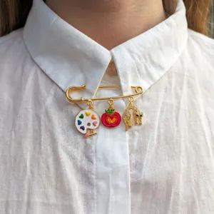 Gros plan d'une broche épingle dorée avec des breloques artistiques sur une chemise blanche.