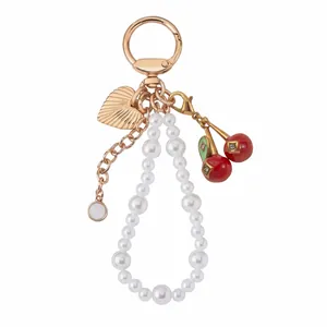 Dettaglio di un elegante ciondolo per borsa con perle bianche e pendente a forma di ciliegia rossa