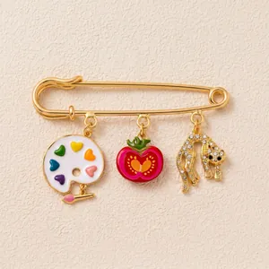 Détail d'une broche épingle à nourrice dorée avec breloques palette et léopard stylisées