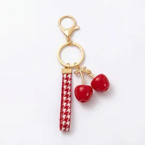 Detail of cute red cherry keychain with houndstooth strap and gold hardware.