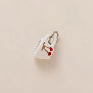 Dettaglio di un ciondolo a forma di tazzina bianca con motivo a ciliegia rossa e anello.