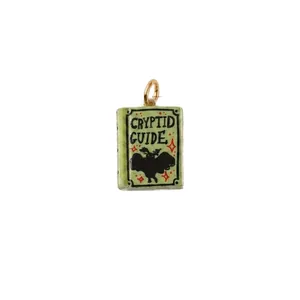 Green Cryptid Guide book pendant with mothman illustration on white background