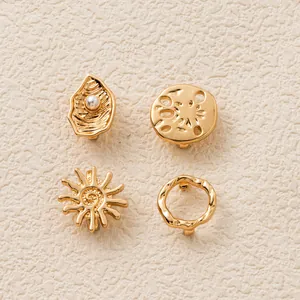 Detailansicht von vier goldfarbenen Deko-Anhängern für Sandalen in Sonnen- und Muscheldesign.