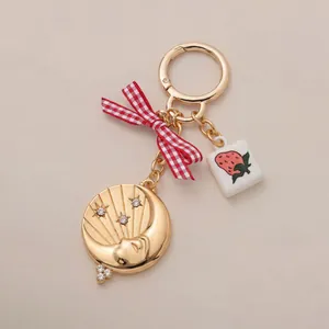 Detail of a gold-plated keychain with crescent moon, red bow, and strawberry charm