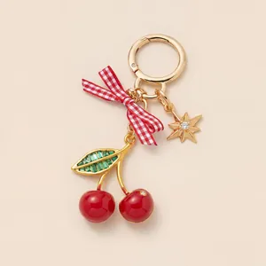 Detailed close-up of a gold cherry keychain with red gingham bow and green crystal leaves