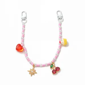 Detail of pink beaded bag charm with red heart and cherry pendants on white background