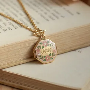 Close-up van gouden achthoekige MOM medaillon met bloemig emaille op een oud boek.