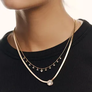 Close-up view of a layered gold necklace featuring a zircon solitaire on a model.