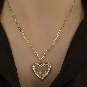 Gros plan sur un collier médaillon cœur doré irrégulier avec breloques soleil et lune