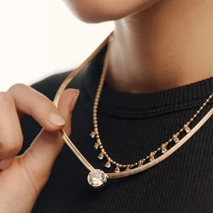 Detailed close-up of layered gold herringbone chain and zircon drop necklace.