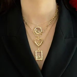 Gros plan de colliers médaillons superposés en forme de cœur et carré en or 18 carats.