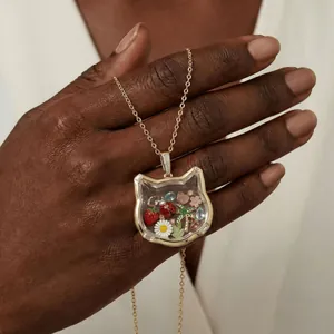 Gros plan d'un pendentif médaillon en verre en forme de chat avec des charms
