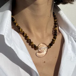 Nahaufnahme einer Tigerauge-Perlenkette mit einem nautischen Muschelanhänger als Detail.
