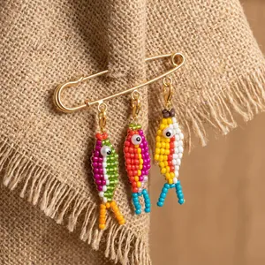 Close-up of handmade beaded fish charms on a golden safety pin brooch with burlap background