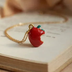 Macro detail of a bitten apple pendant on a gold chain over a vintage book.
