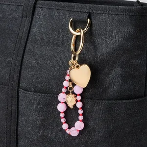Detailansicht eines rosa Perlenherz- und Erdbeeranhängers an einer strukturierten schwarzen Tasche.